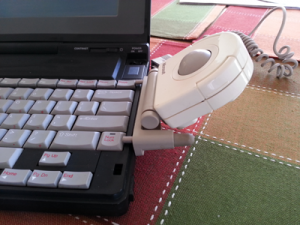 Figure 2. The Microsoft Ballpoint mouse clamped to the side of an NEC Ultralite, vintage 1989 laptop.